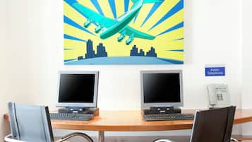 A workspace with two monitors, a public telephone, and a cityscape painting.