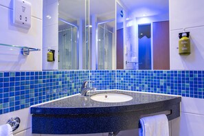 A bathroom with a blue-tiled backsplash, a granite countertop sink, a mirror, and a towel rack.