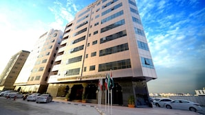 A modern multi-story hotel with a prominent entrance and several flags. - Emirates Stars Hotel Apartments Sharjah (Sharjah)