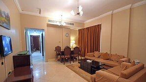 A living room with a sofa, coffee table, TV, and a dining area with chairs and a table. - Emirates Stars Hotel Apartments Sharjah (Sharjah)