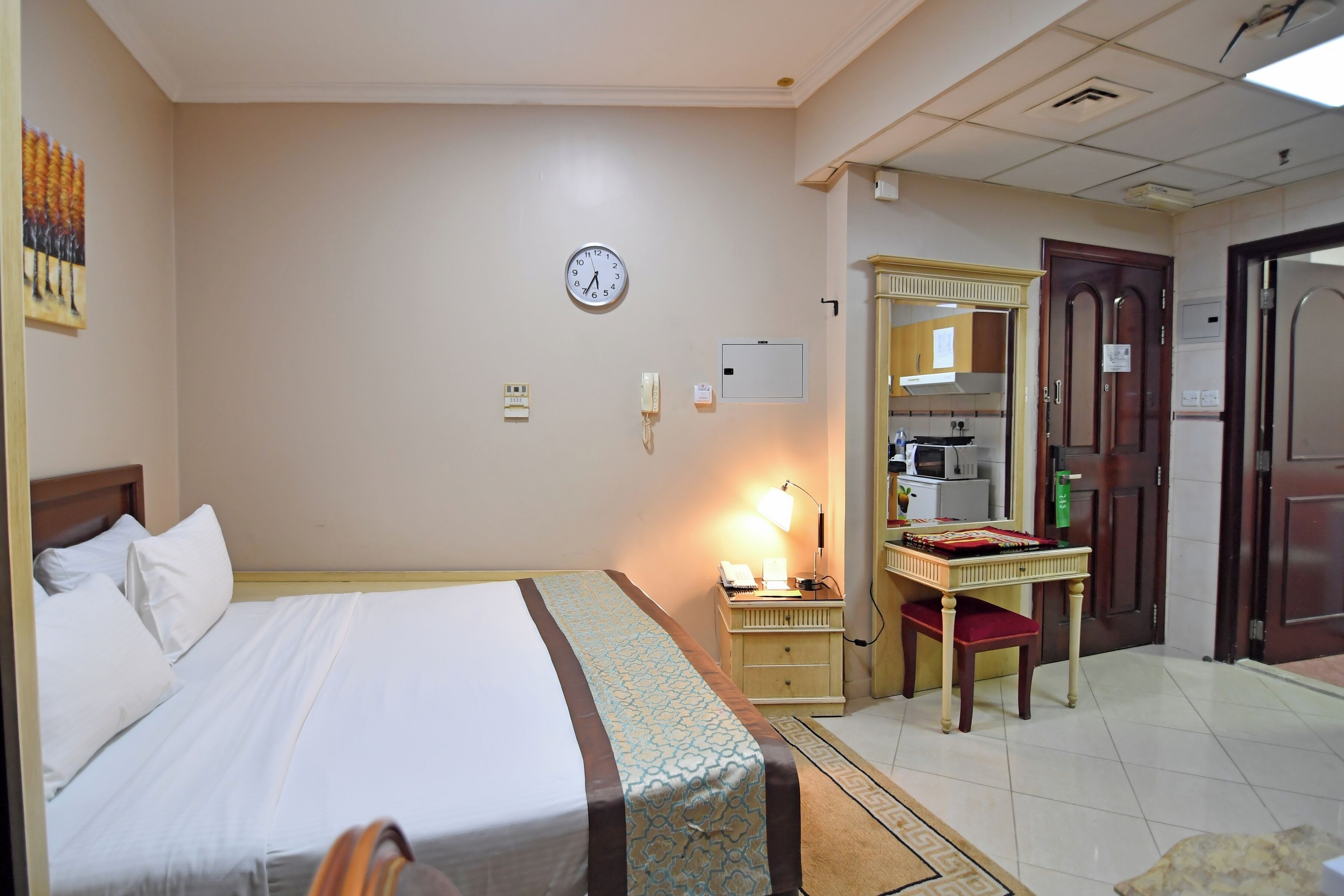Hotellihuone, jossa on sänky, kirjoituspöytä lampun kanssa, seinäkello ja peili.