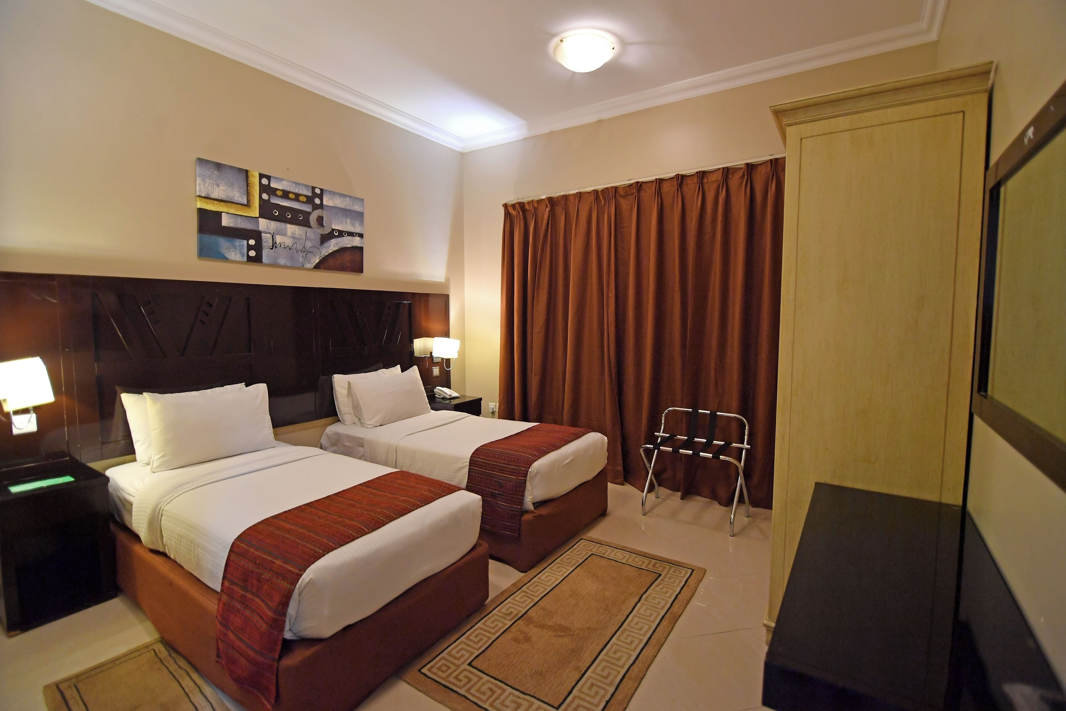 A hotel room with two beds, a desk, a chair, a television, and a painting on the wall.