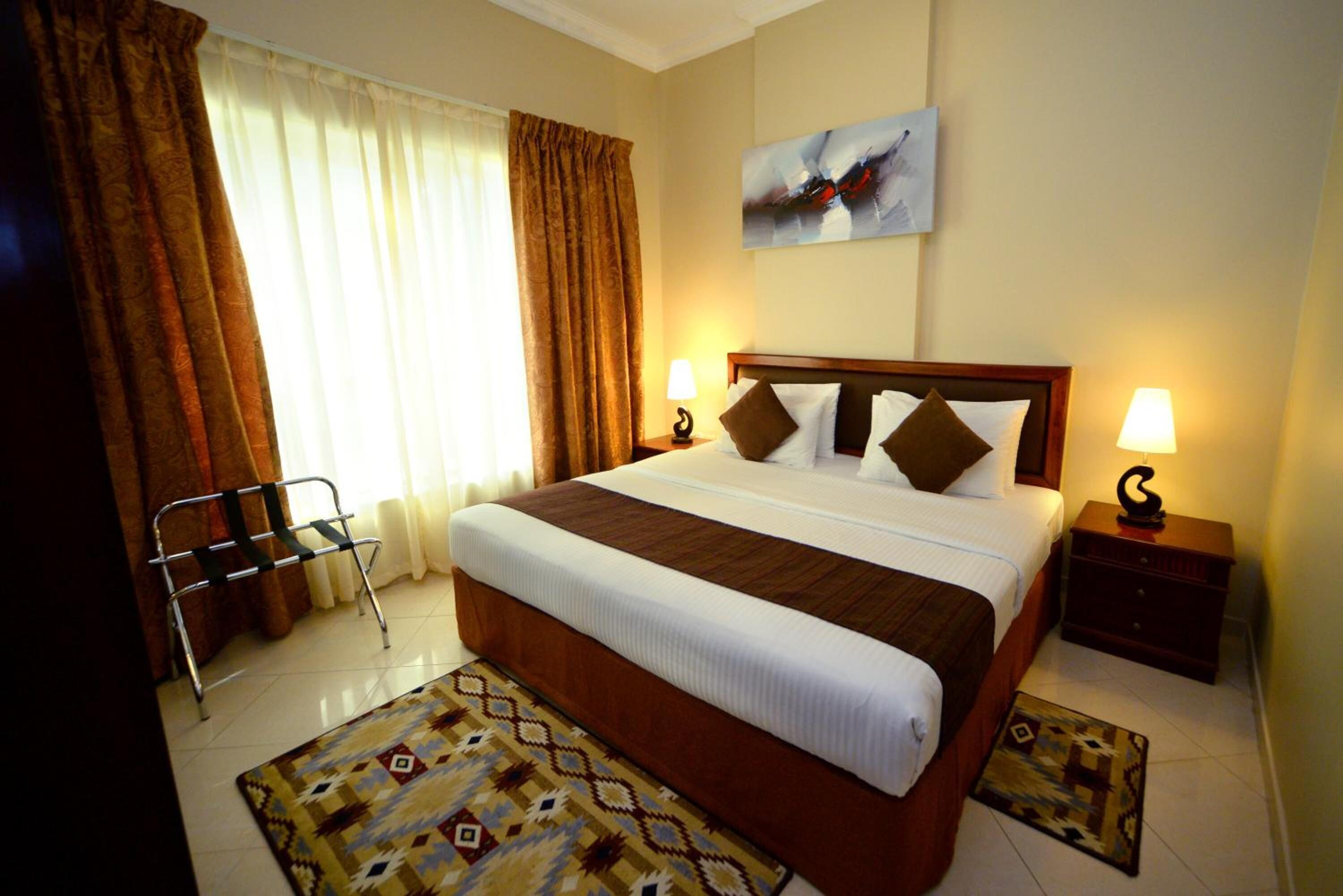 A hotel room with a large bed, two bedside tables, a chair, and a window with curtains.