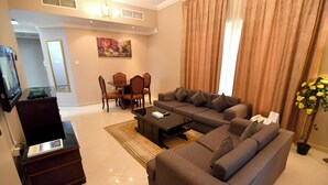 A modern living room with a sectional sofa, a coffee table, and a dining area with chairs and a table. - Emirates Stars Hotel Apartments Sharjah (Sharjah)