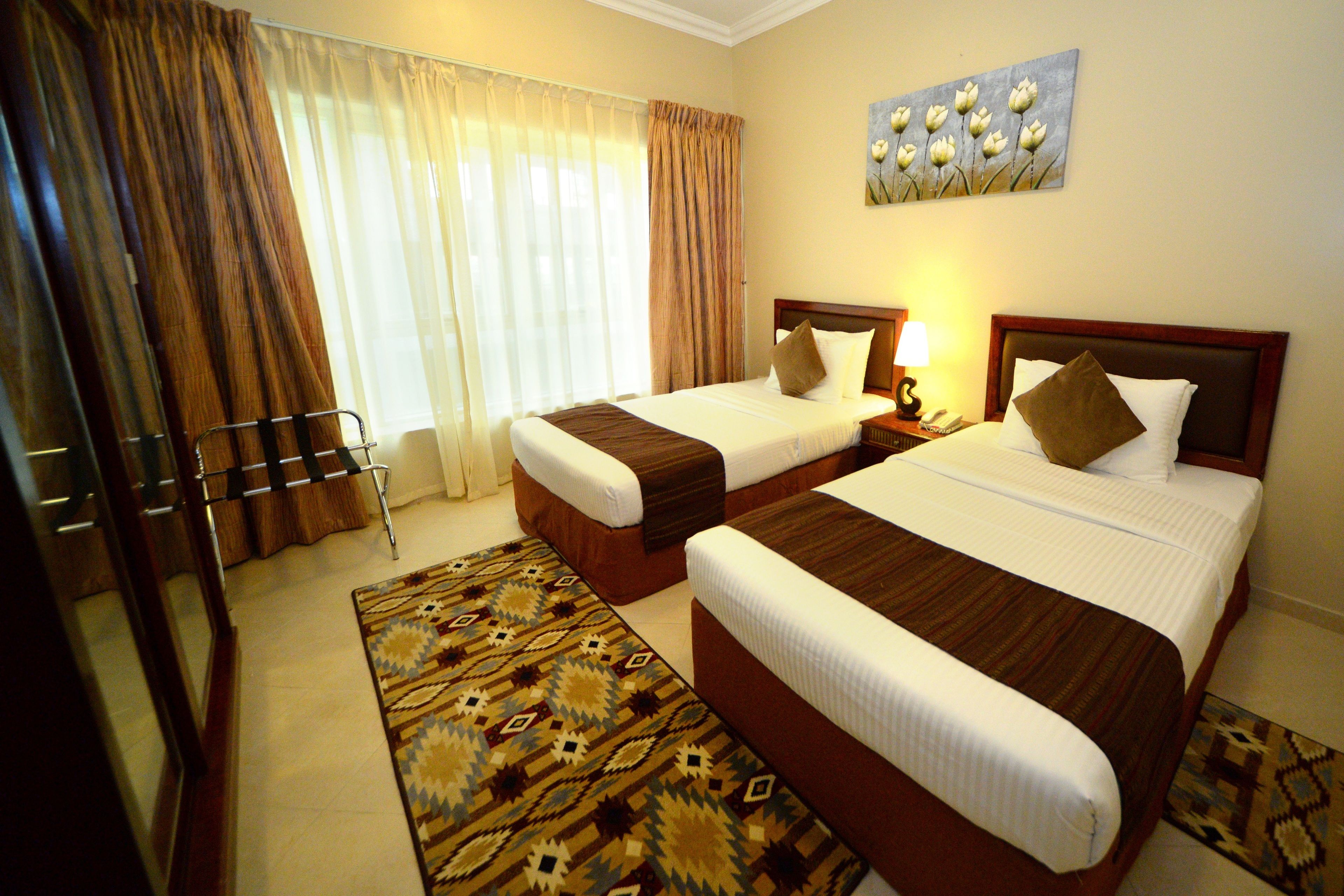 Habitación de hotel con dos camas, un ventanal con cortinas, un cuadro en la pared y una alfombra estampada.