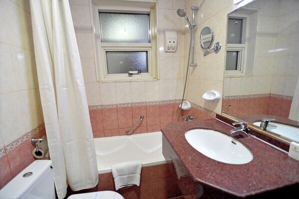 A bathroom with a bathtub, two sinks, a shower, a toilet, and a window.