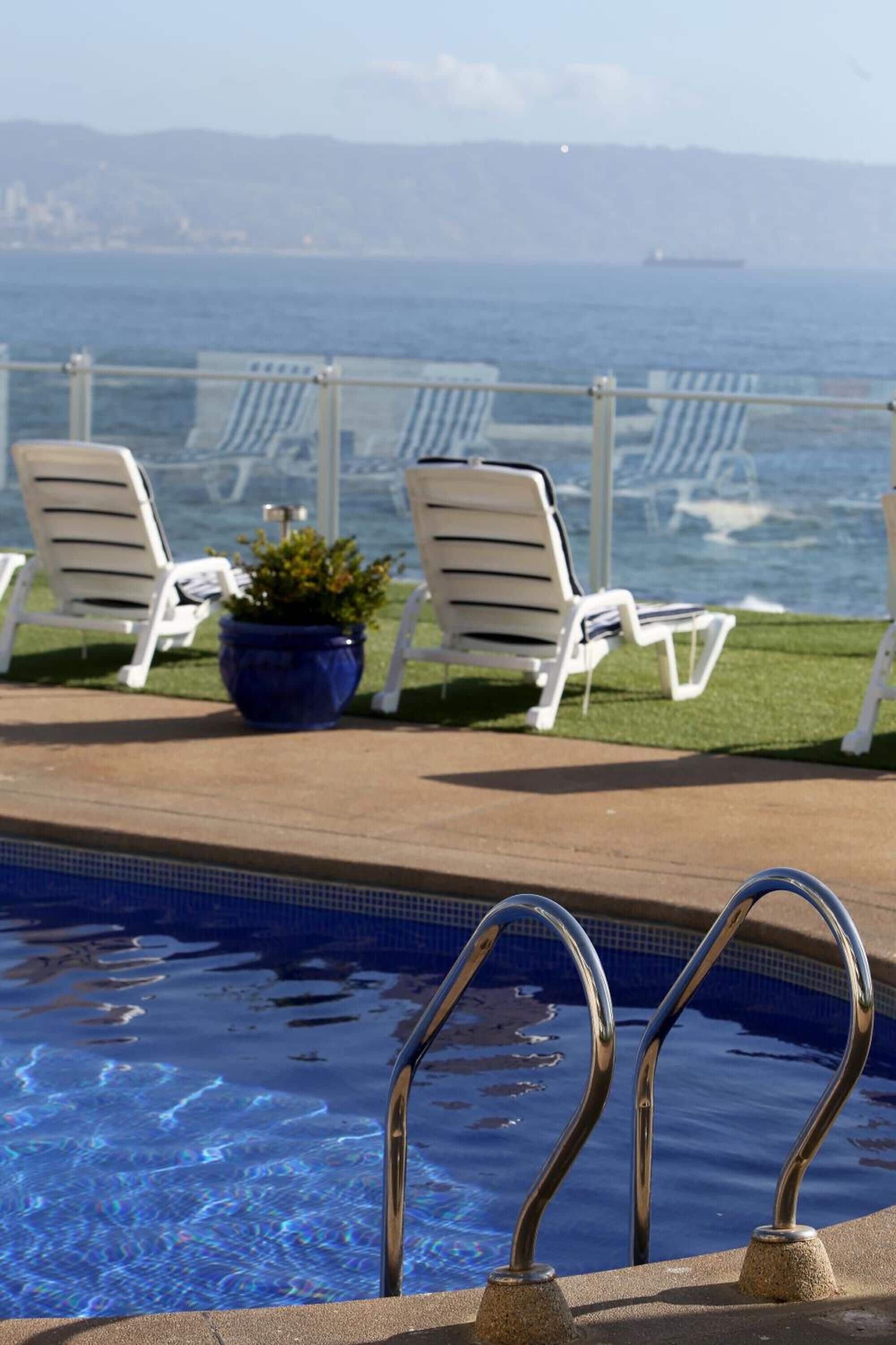 Un área junto a la piscina con sillones de descanso y una planta en maceta.