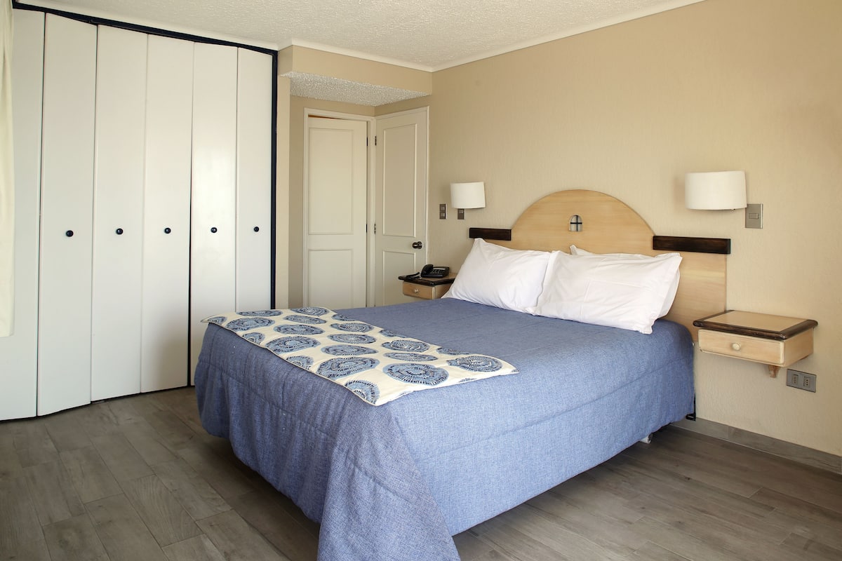 A hotel room with a bed, bedside tables, a wardrobe, and a door.