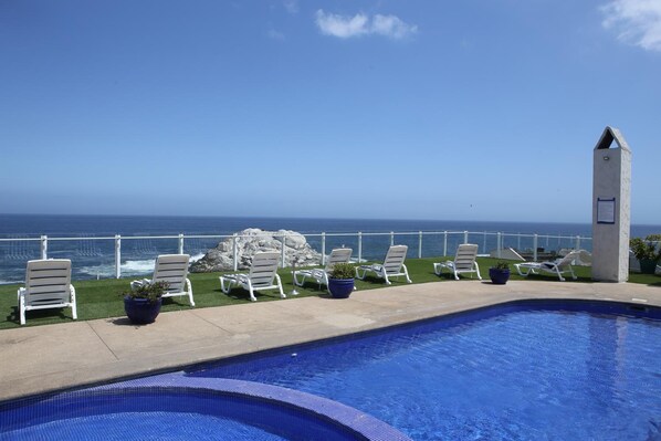 A swimming pool with a view of the ocean, surrounded by lounge chairs and potted plants.