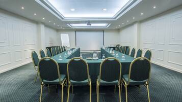 A conference room with a long table, chairs, a projector screen, and a whiteboard.