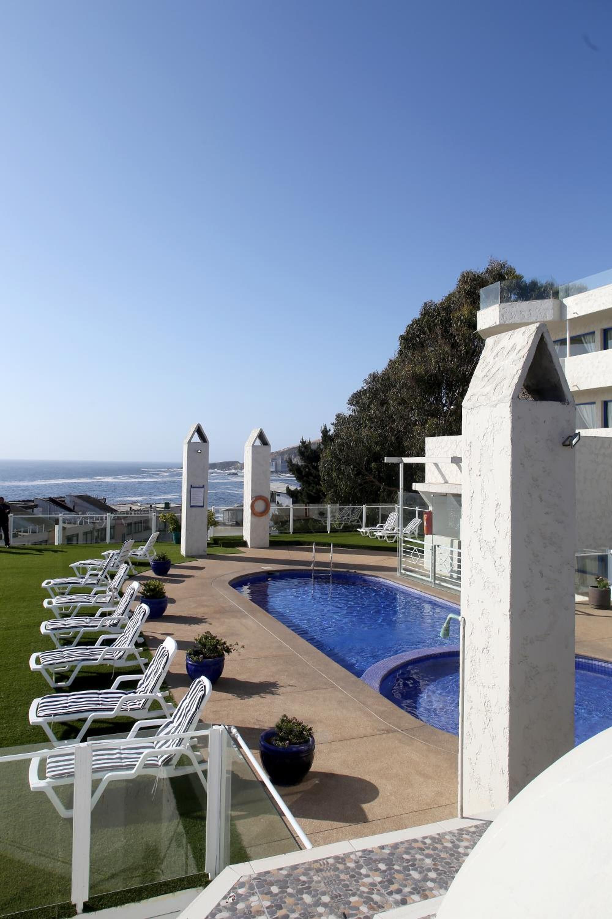 A pool area with lounge chairs, a clear view of the ocean, and a modern building structure.