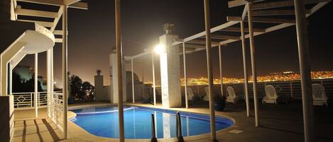 A nighttime swimming pool area with a view of a cityscape.