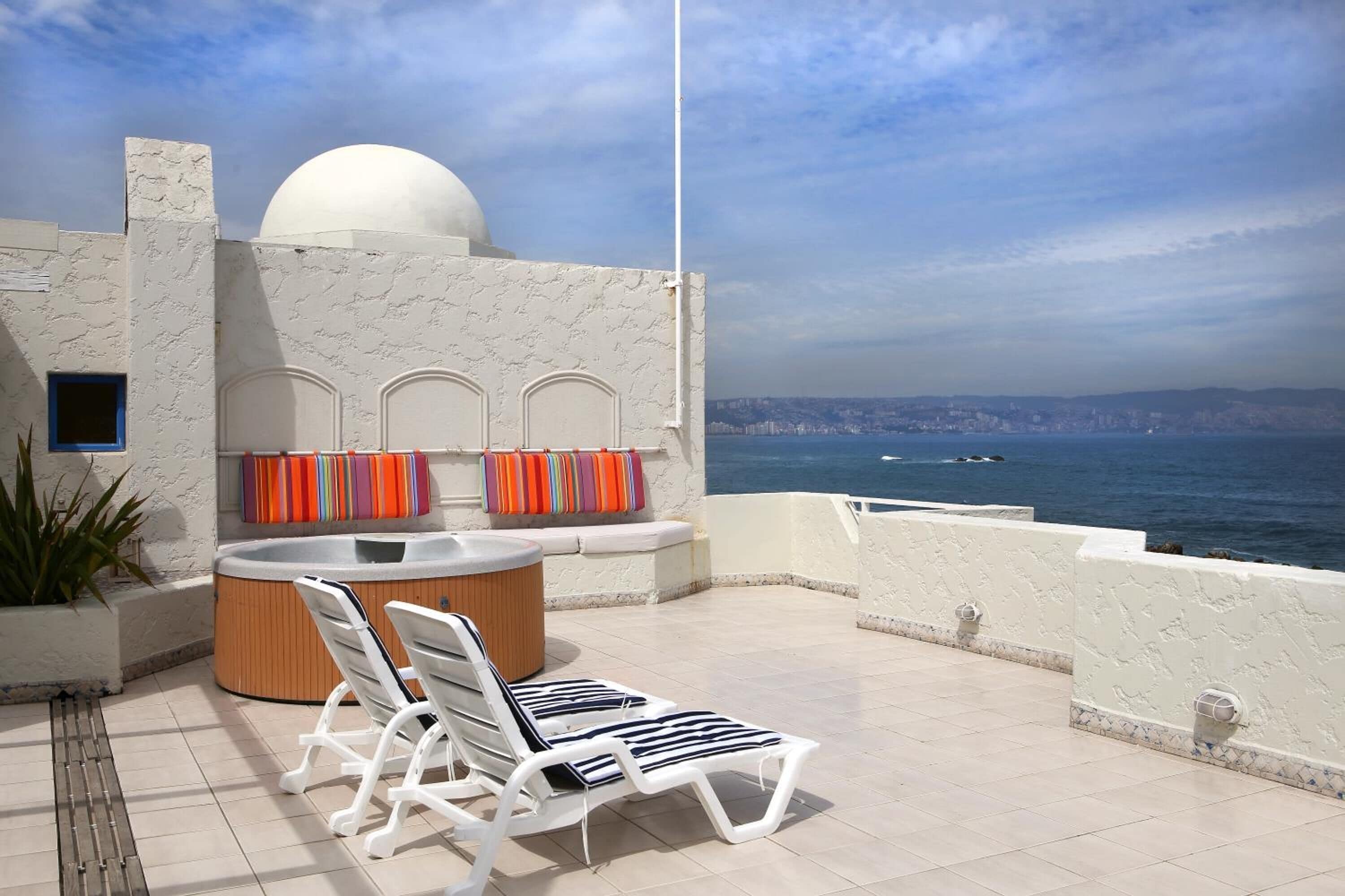 Una terraza en la azotea con jacuzzi, sillas de descanso y vista al mar.