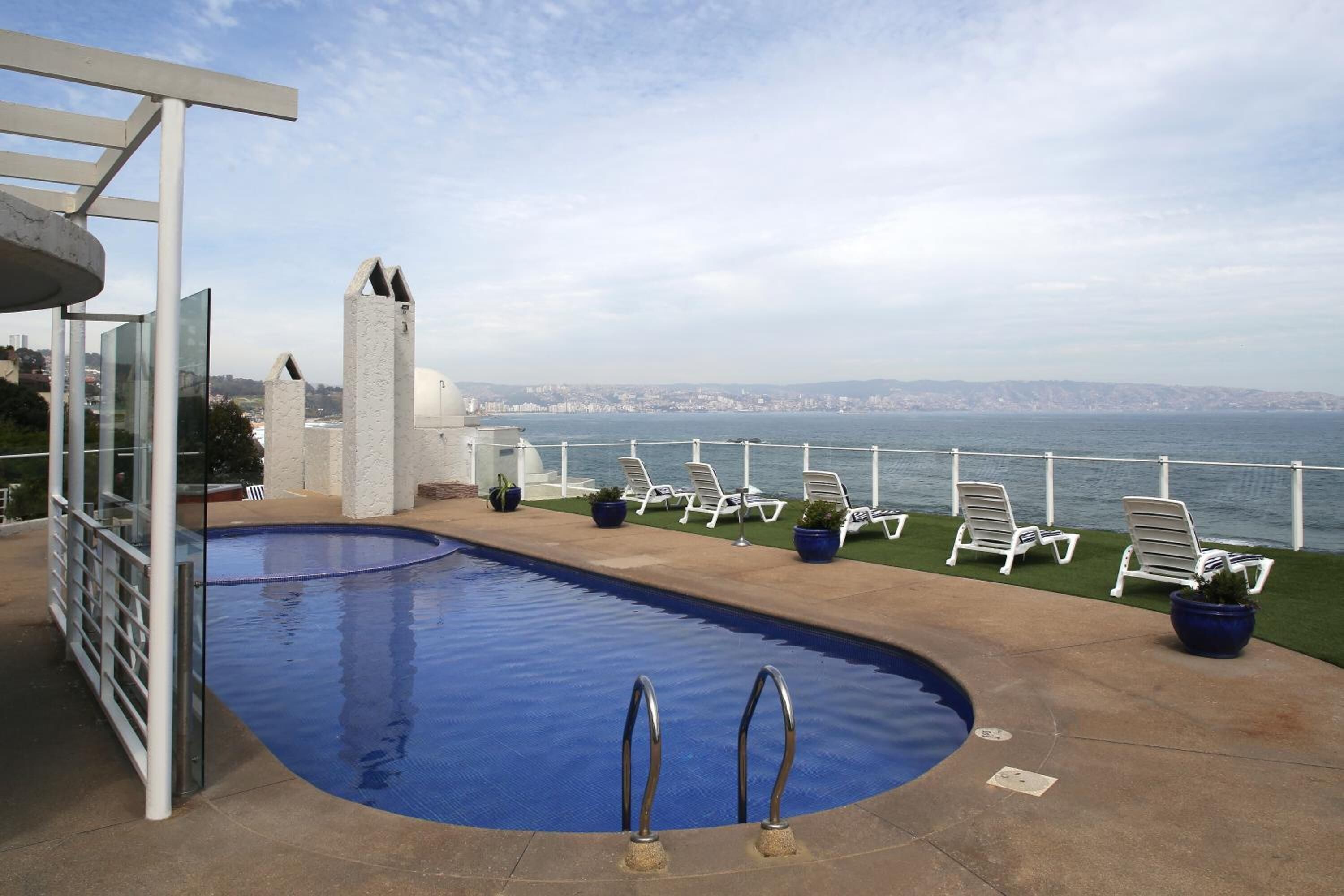 Una piscina con vista al mar, sillas de descanso y una estructura arquitectónica moderna.