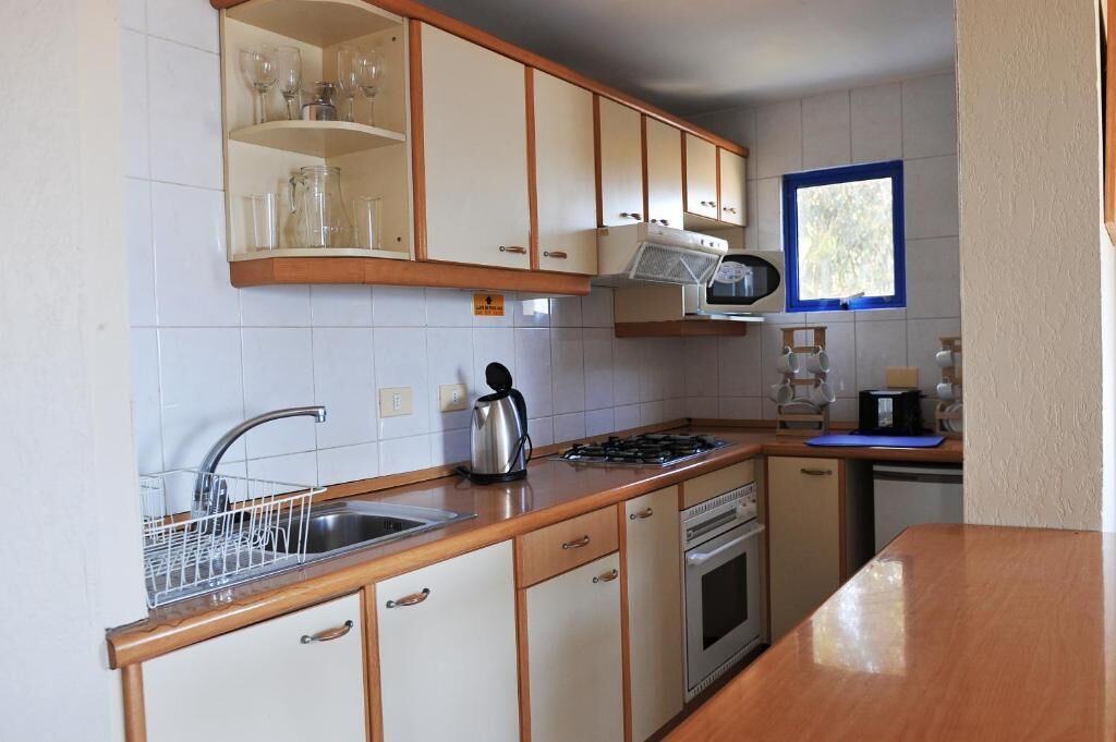 A compact kitchen with white cabinets, a stainless steel sink, a kettle, and a microwave.