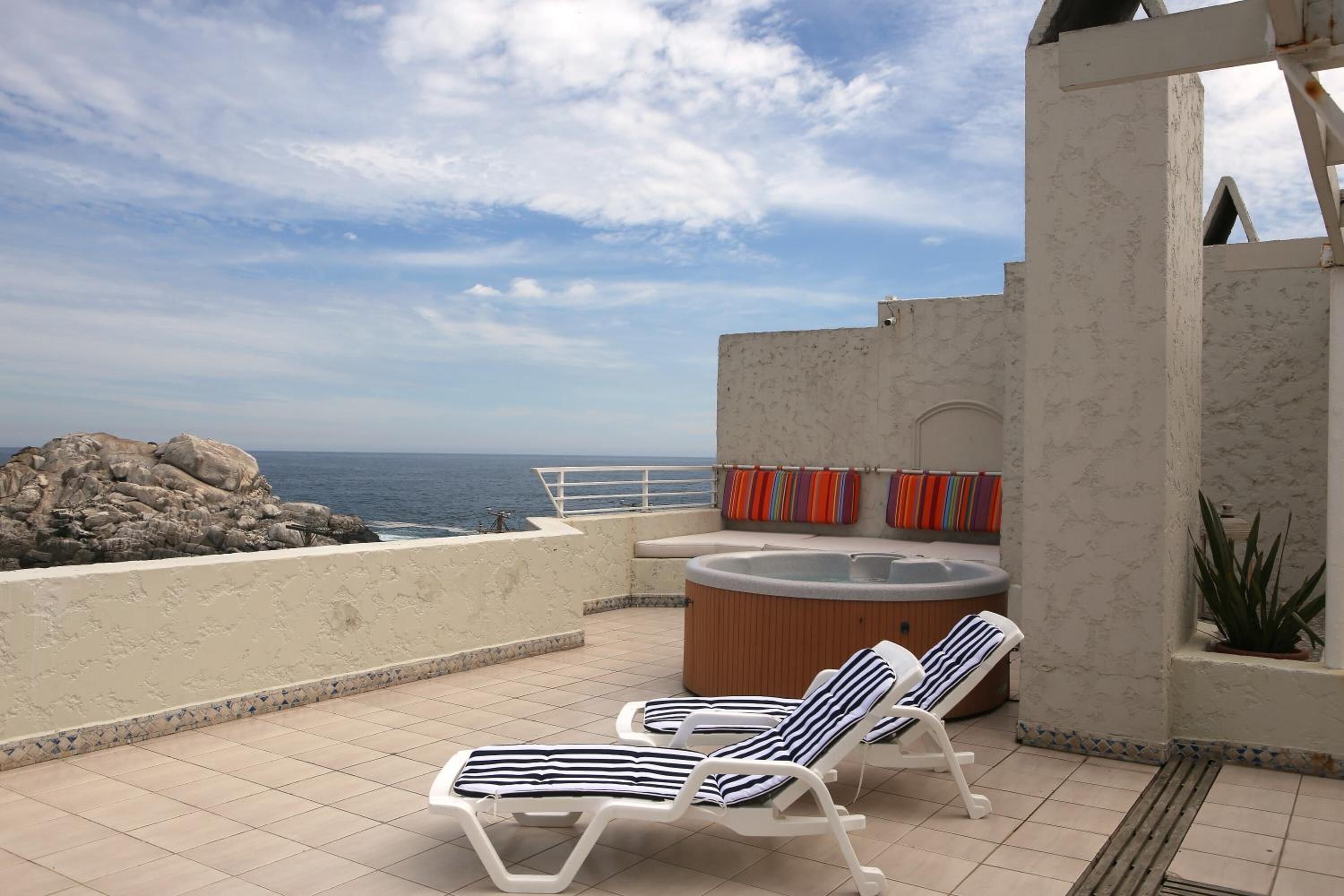 Una terraza en la azotea con dos tumbonas, un jacuzzi y vista al océano.