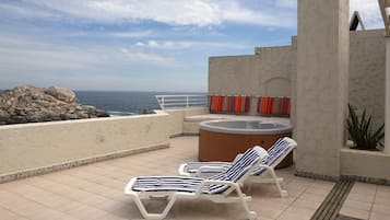 A rooftop terrace with two sun loungers, a hot tub, and a view of the ocean.
