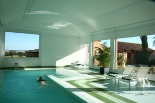 Una piscina interior con vistas al campo, una fuente de agua y sillas de descanso.