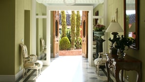 A hallway with a marble floor, a wooden chair, a table with a lamp, and a mirror on the wall. - Valdepalacios (Torrico)