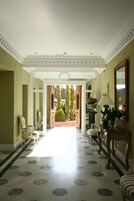 A hallway with a marble floor, a wooden chair, a table with a lamp, and a mirror on the wall.