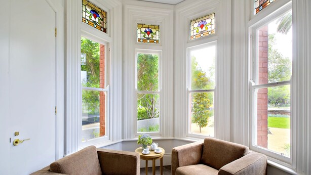A room with two brown armchairs, a small round table with a white teapot and cups, and a large window with stained glass.