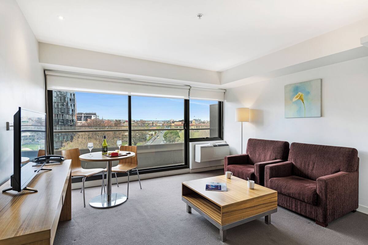 A modern hotel room with a large window, a sofa, a coffee table, and a desk with a chair.