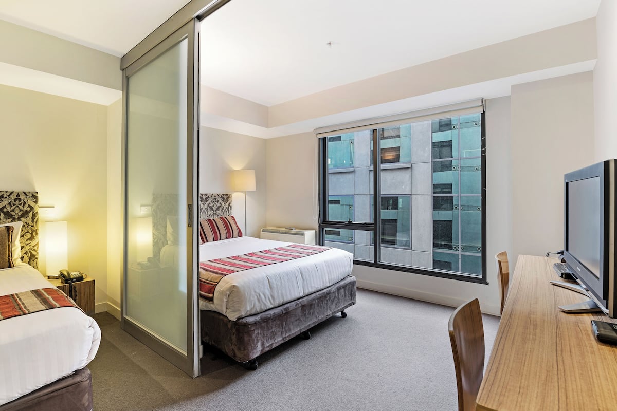 A hotel room with a bed, a desk, a TV, and a large window.