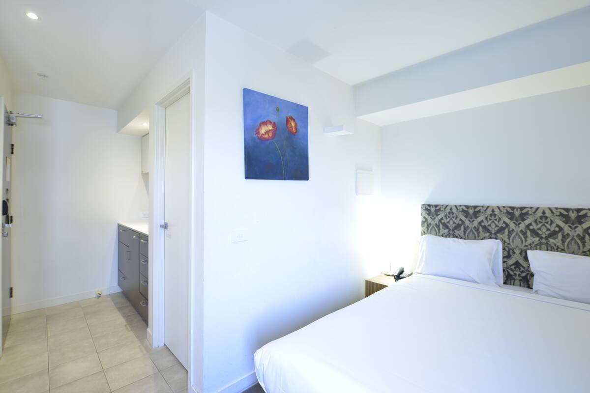 A hotel room with a bed, a nightstand, a painting, a bathroom, and a wardrobe.