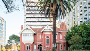 A historic red brick building with a central entrance, surrounded by modern high-rise buildings.