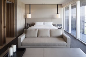 A modern hotel room with a large bed, a sofa, and a view through large windows.