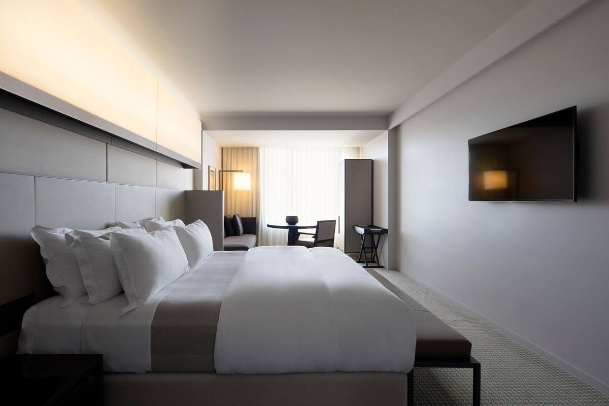 A modern hotel room with a large bed, a flat-screen TV, a desk, and a chair.