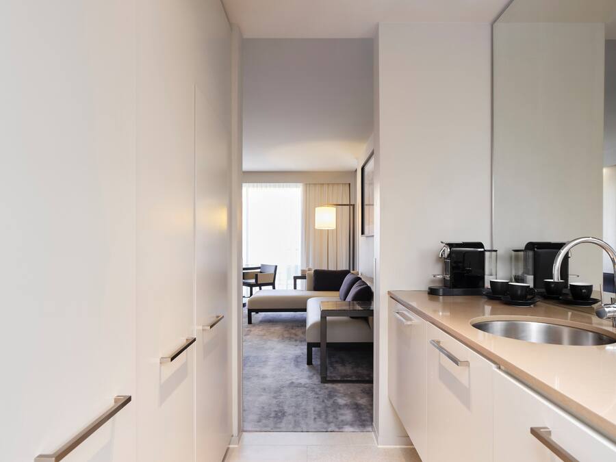 Ett modernt hotellrum med ett litet kök, en matplats med soffa och stolar samt ett stort fönster med gardiner.