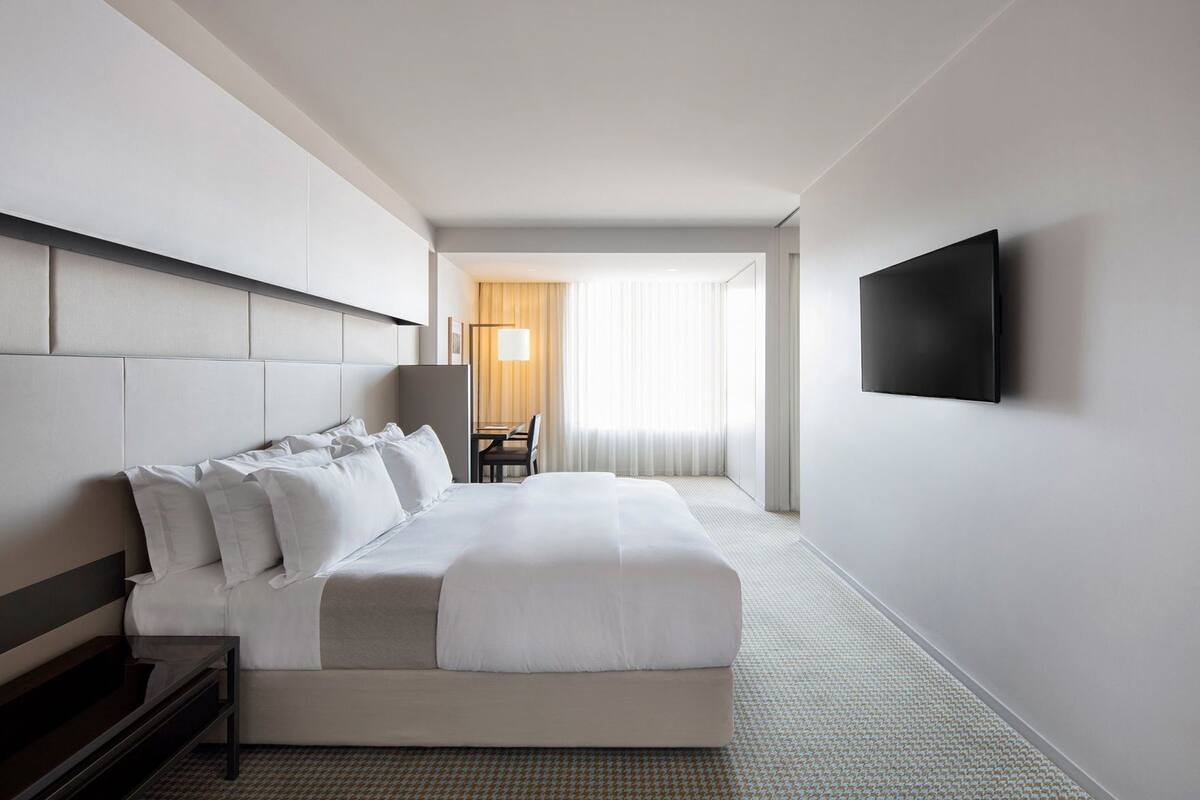 A hotel room with a large bed, a desk, a chair, and a TV mounted on the wall.