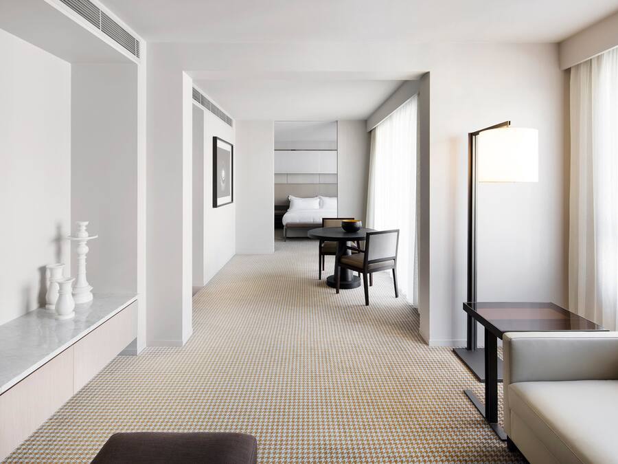 Ein Hotelzimmer mit modernem Design, das eine Sitzecke, einen Esstisch mit Stühlen, eine Lampe und ein Bett im Hintergrund beinhaltet.