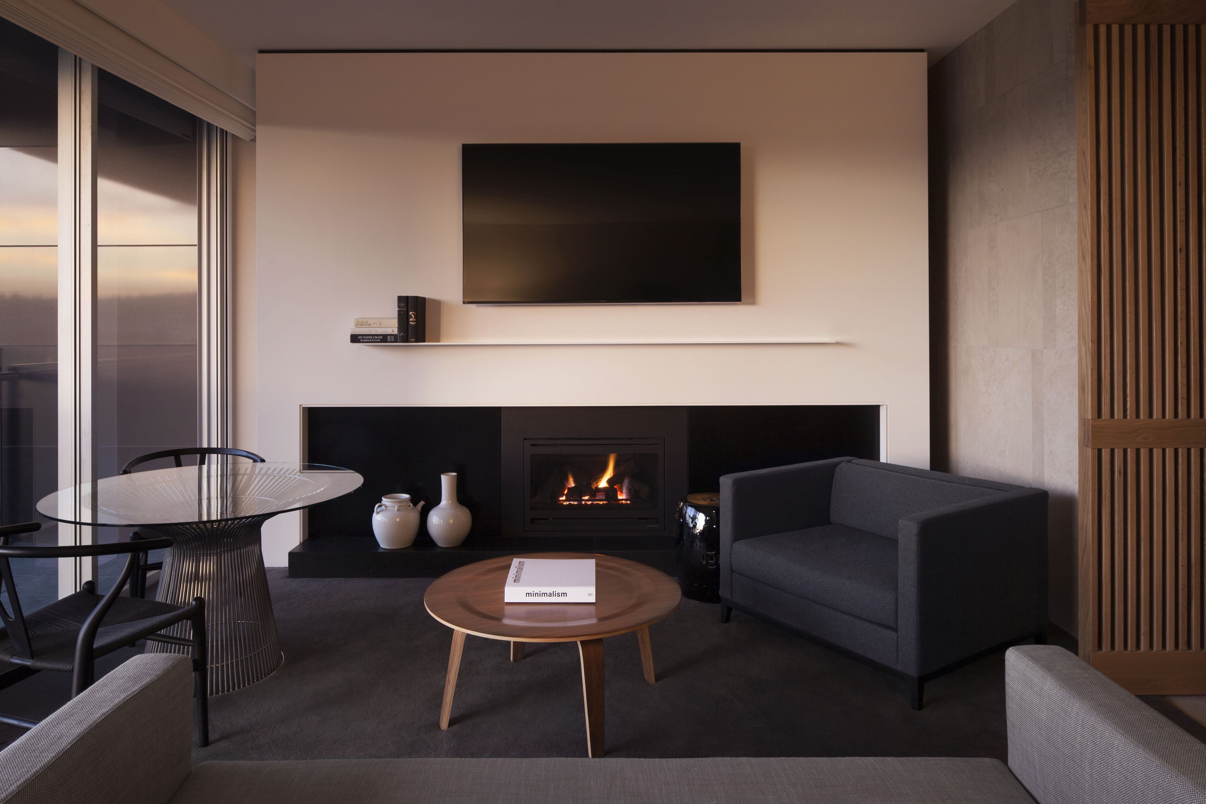 A modern living room with a fireplace, a flat-screen TV mounted above it, a round coffee table with a book, and a sofa.