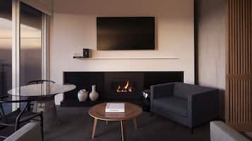 A modern living room with a fireplace, a flat-screen TV mounted above it, a round coffee table with a book, and a sofa.