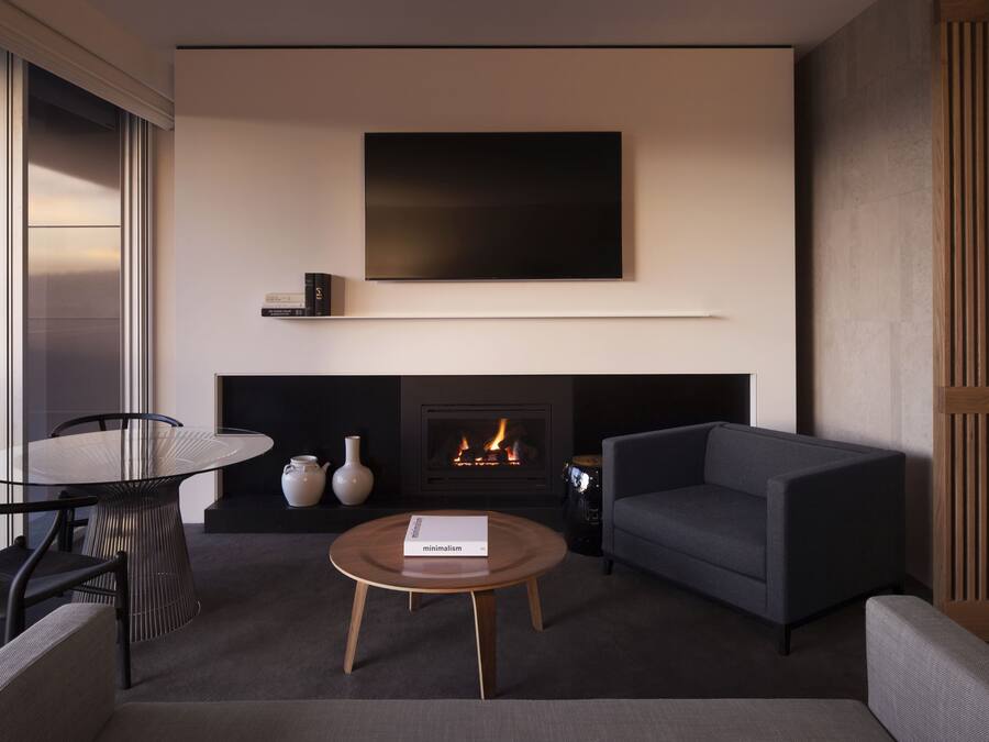 A modern living room with a fireplace, a flat-screen TV mounted above it, a round coffee table with a book, and a sofa.