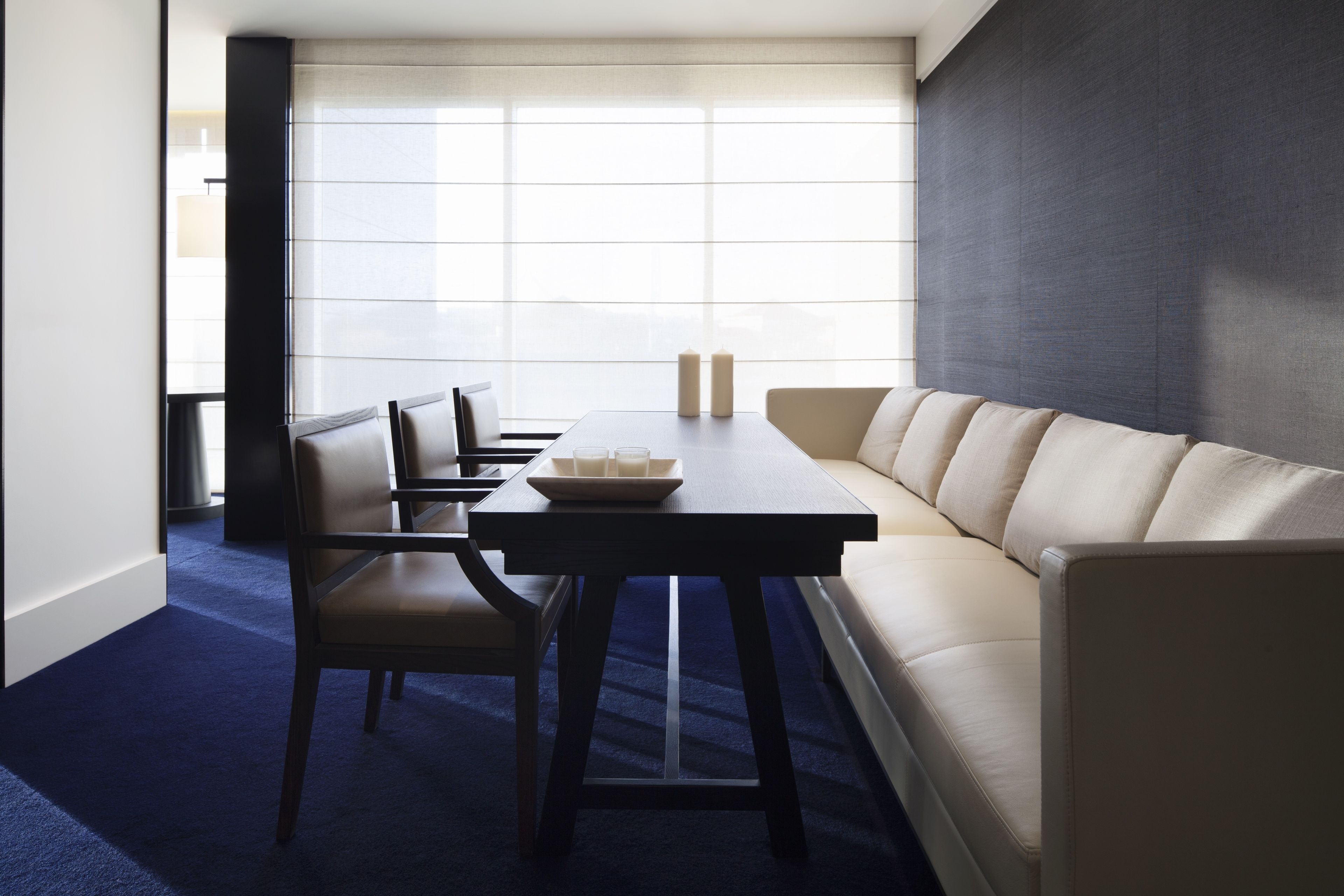 Una sala moderna con un sofá, una mesa de comedor con sillas y un ventanal que proporciona luz natural.