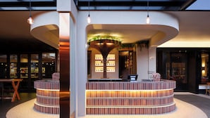 A modern lobby with a central reception desk, a curved seating area, and a glass ceiling. - Hotel Realm (Barton)