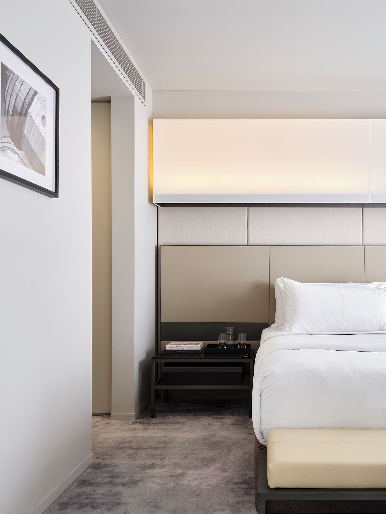 Ein modernes Hotelzimmer mit einem großen Bett, einem Nachttisch mit Lampe, einem gerahmten Bild an der Wand und einem großen Fenster.