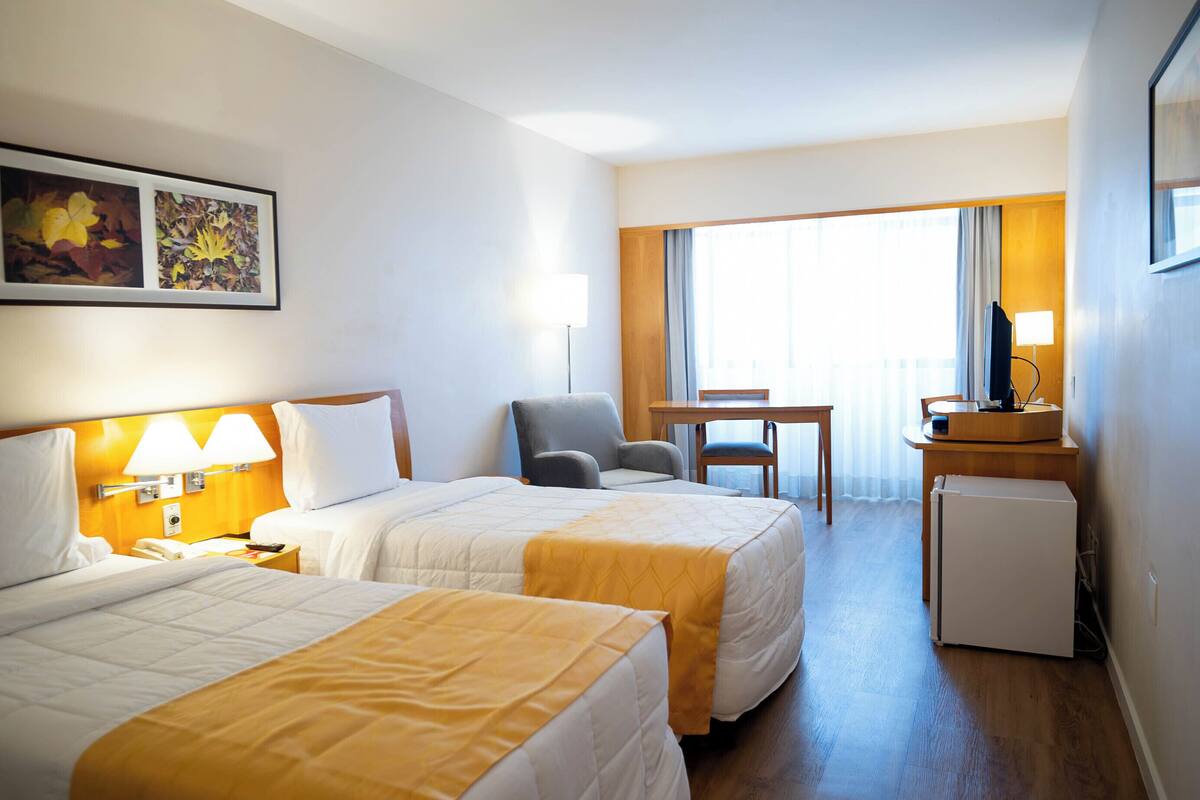 Une chambre d’hôtel avec deux lits, un bureau, une chaise, une télévision et un réfrigérateur.