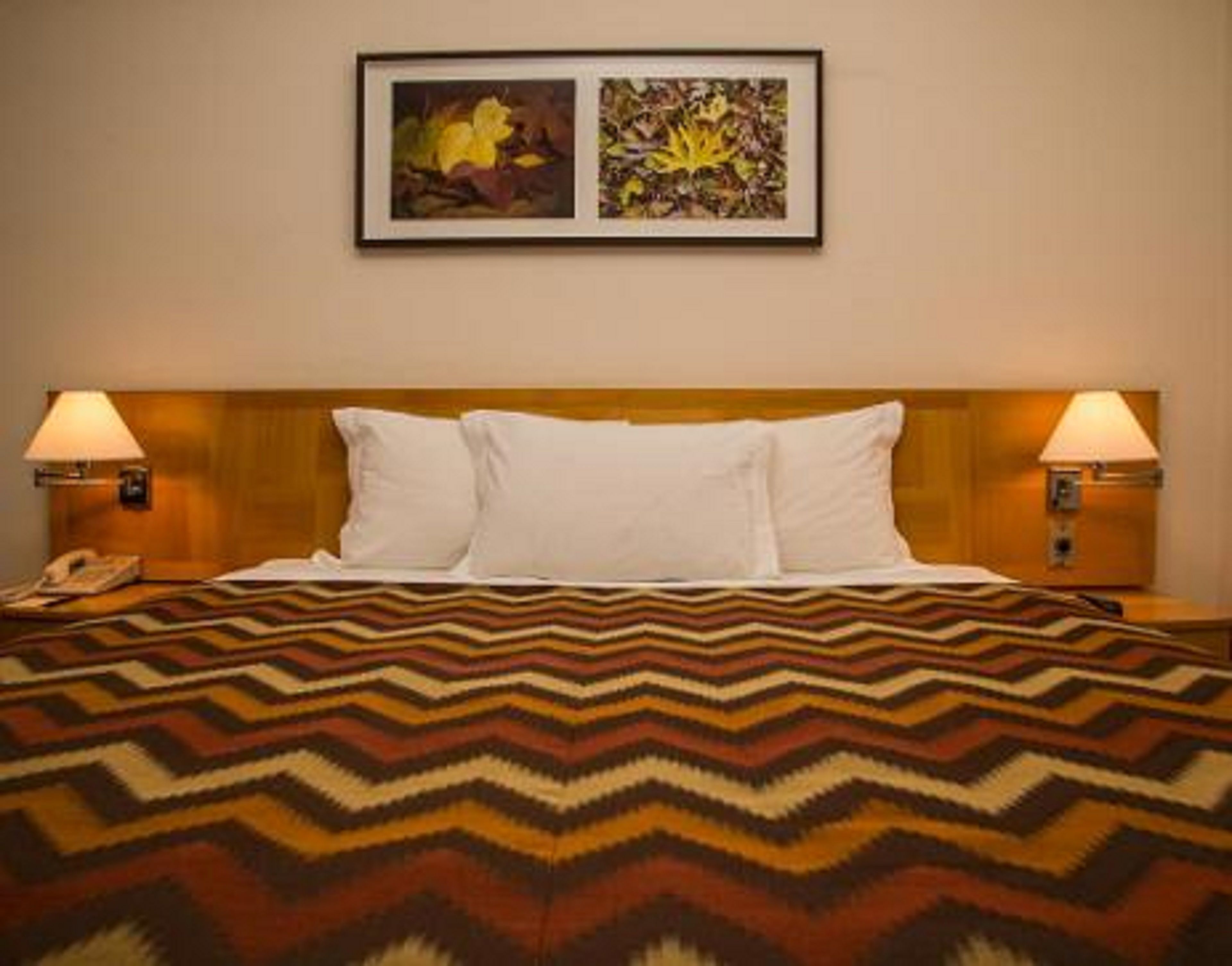A hotel room with a bed, two bedside lamps, and two framed pictures on the wall.