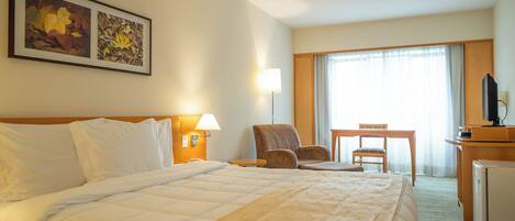 Una habitación de hotel con una cama grande, un escritorio con silla, un televisor y una ventana con cortinas.