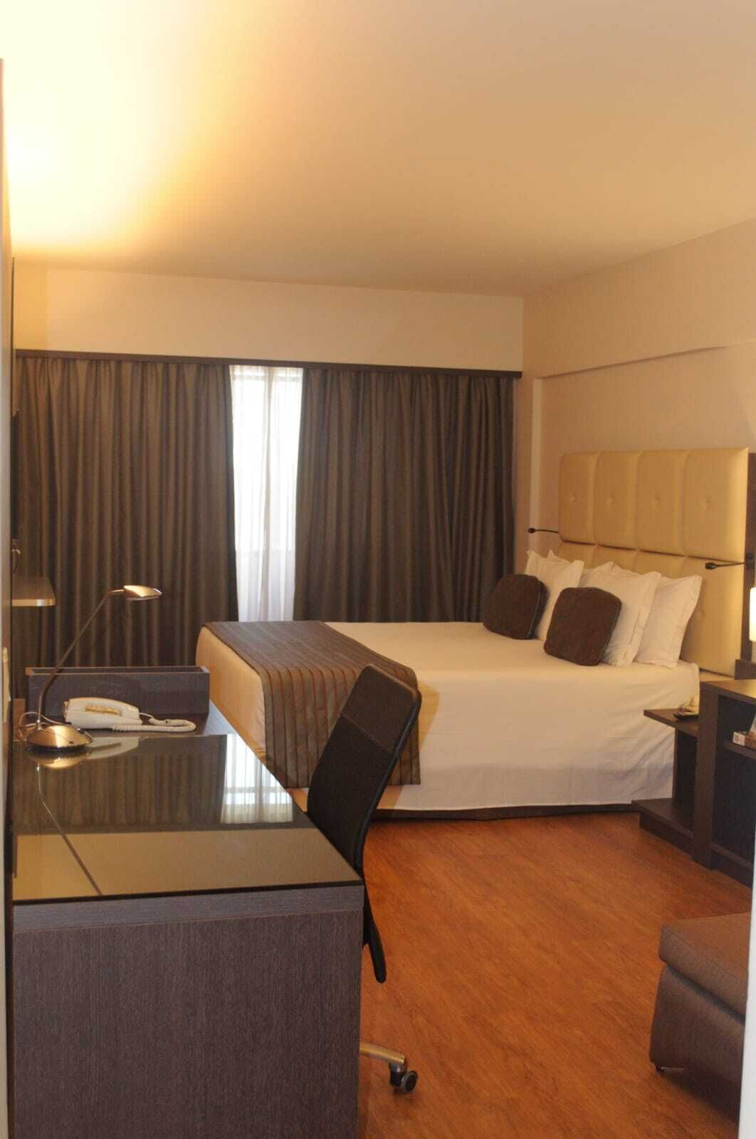 Une chambre d’hôtel comprenant un lit, un bureau avec un téléphone, une chaise, une table de chevet et une lampe.