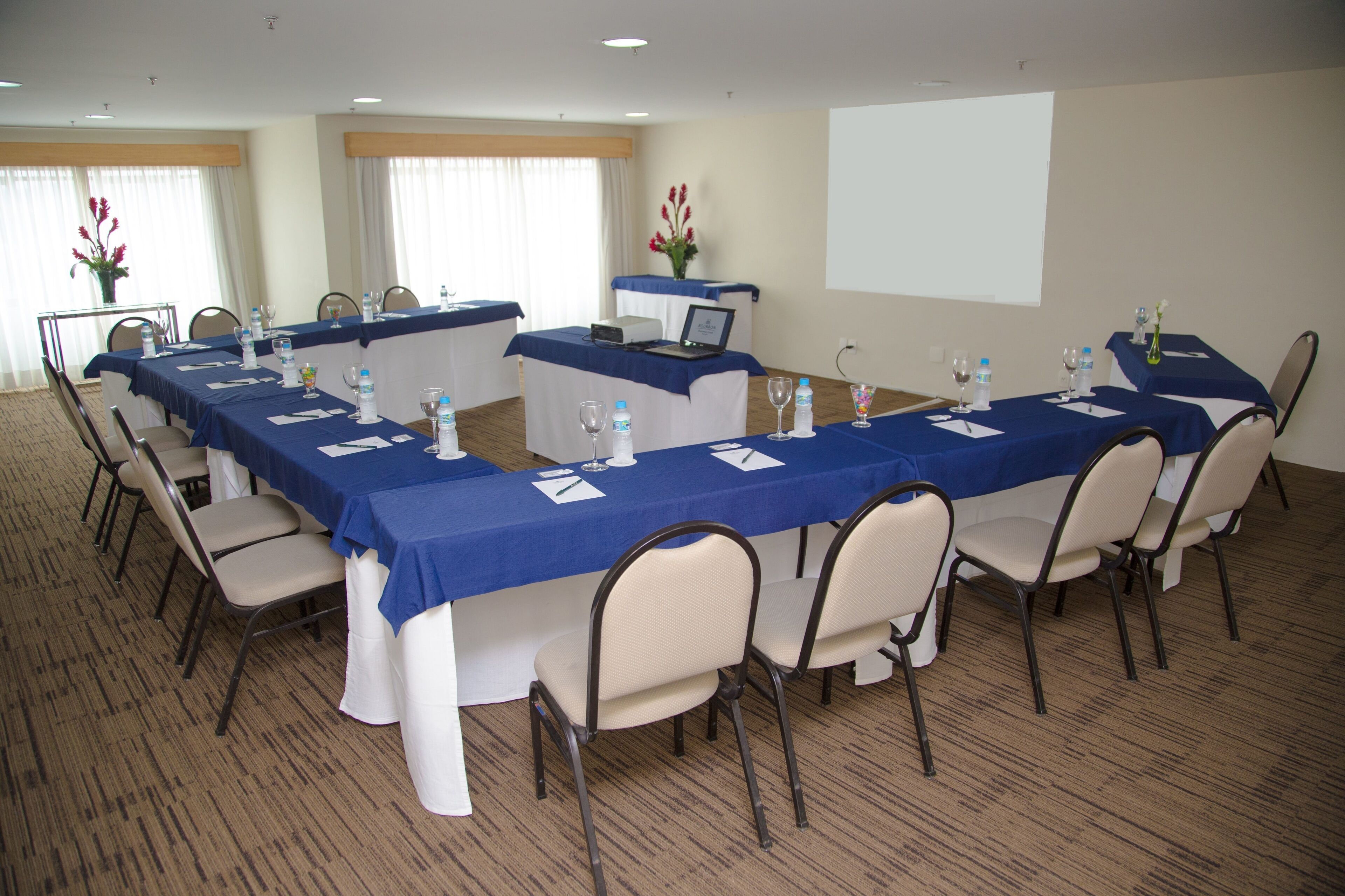 Un salón de conferencias con una larga mesa, sillas, botellas de agua y un ordenador portátil sobre la mesa.