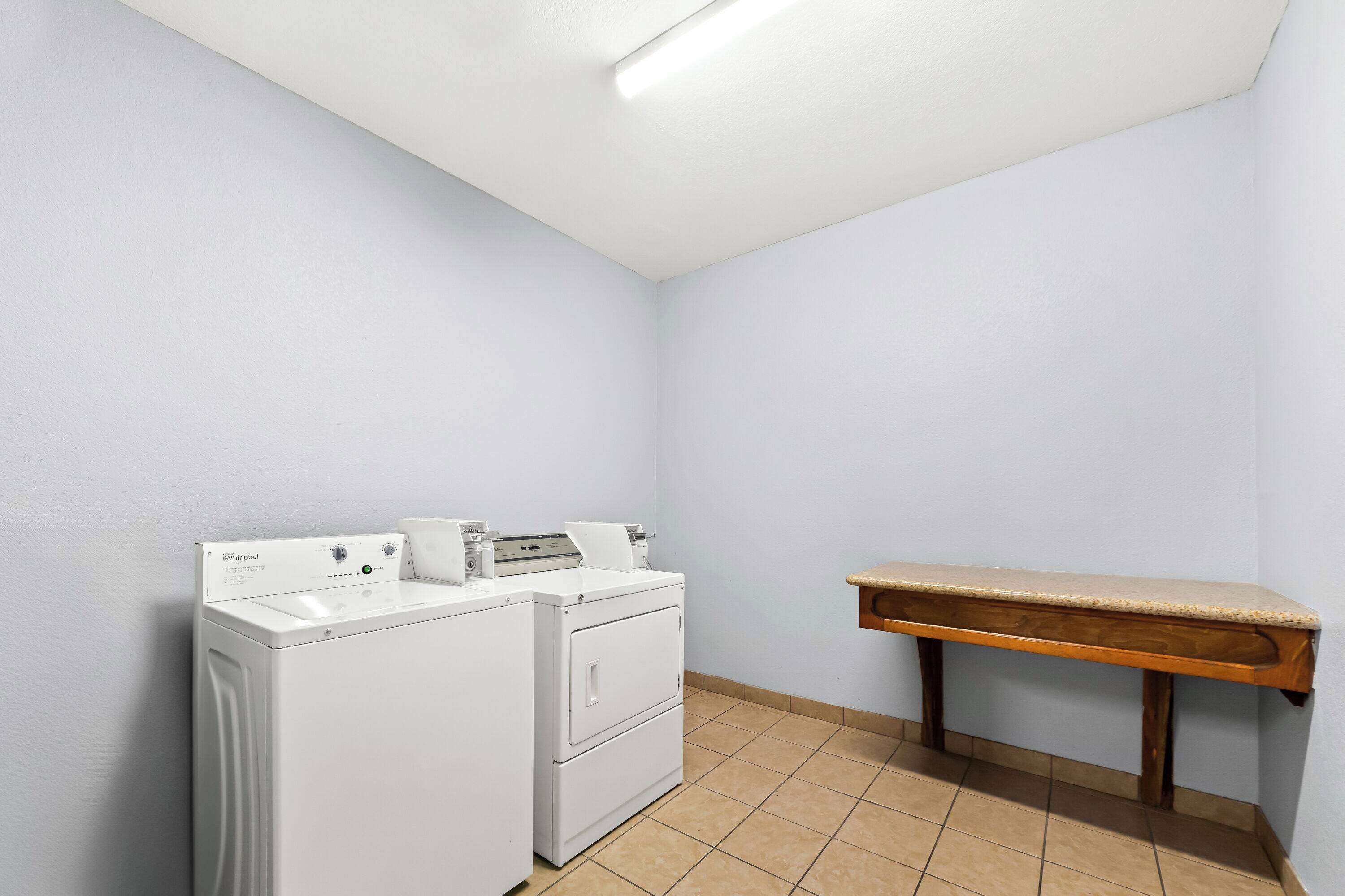 A laundry room with a washing machine and dryer, a wooden bench, and a tiled floor.