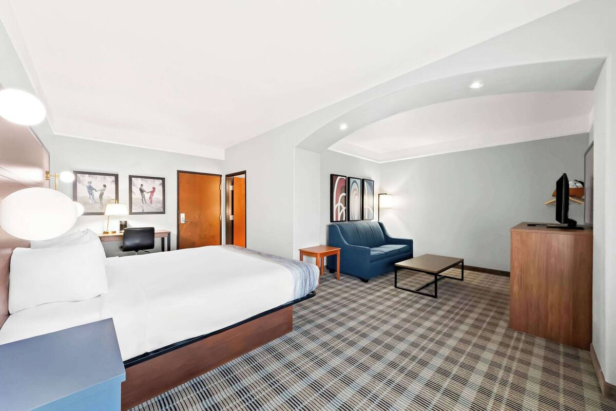 A hotel room with a bed, a blue sofa, a small table, and a TV on a wooden cabinet.