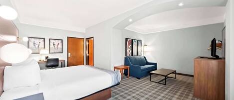 A hotel room with a bed, a blue sofa, a small table, and a TV on a wooden cabinet.