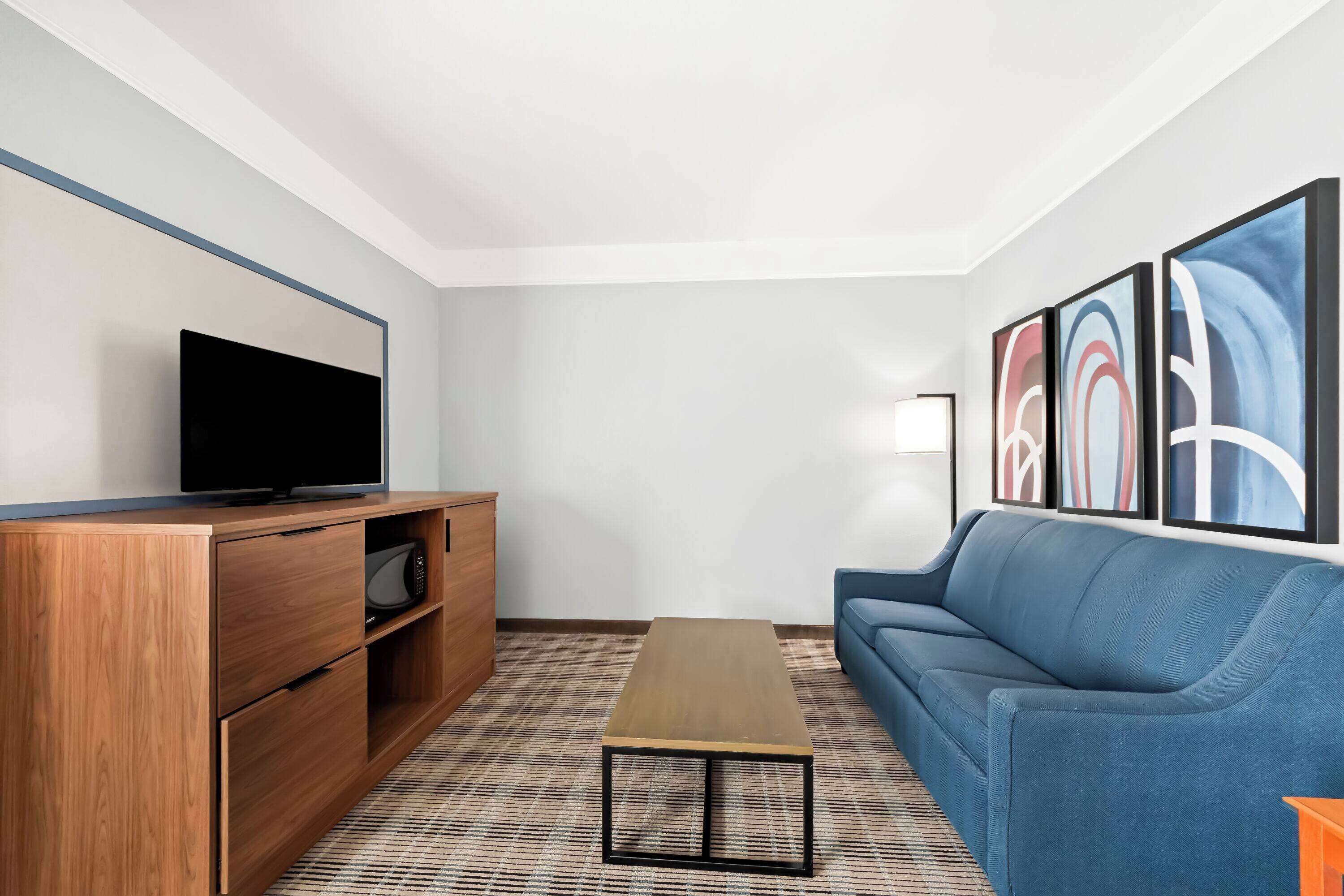 A modern living room with a flat-screen TV, wooden entertainment unit, blue sofa, and abstract wall art.