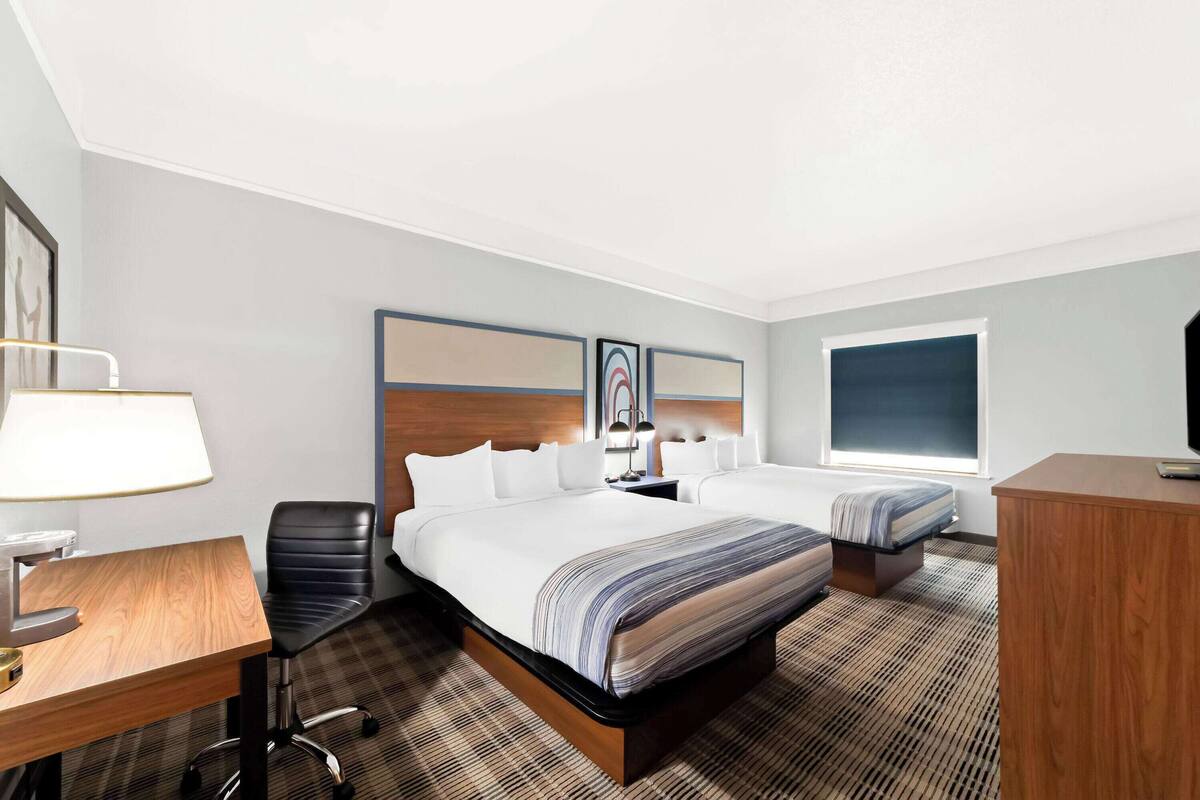 A hotel room with a large bed, a desk, a chair, a TV, and a window.
